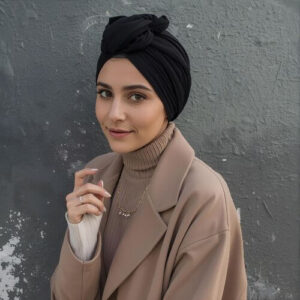 A sleek, modern look featuring a neatly tied turban with a smooth wrap that accentuates the face. This style adds an elegant yet minimalistic feel, paired with a beige coat for a chic and sophisticated appearance.