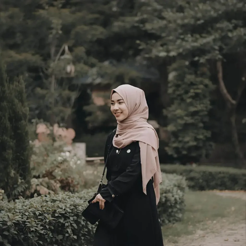 A woman smiling while walking outdoors, dressed in a black hijab and modest attire. This image reflects the essence of what is a hijab, showcasing a chic and modest look, often found in hoor hijab n abayas collections