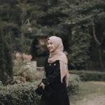 A woman smiling while walking outdoors, dressed in a black hijab and modest attire. This image reflects the essence of what is a hijab, showcasing a chic and modest look, often found in hoor hijab n abayas collections