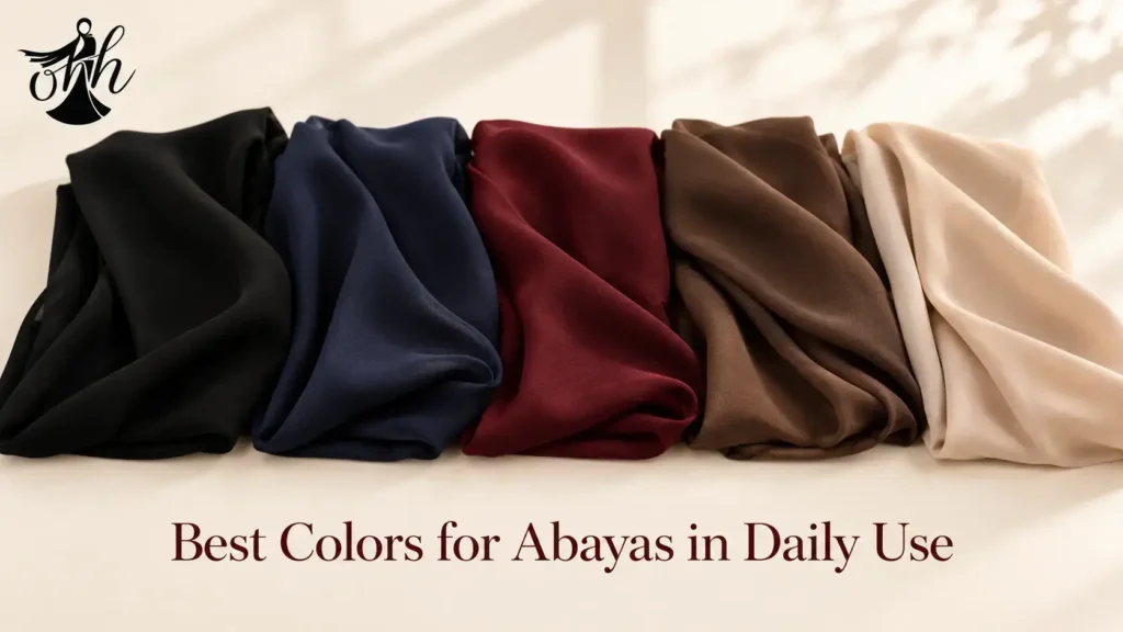 Hoor Hijab & Abayas flat lay showing five folded abaya fabric swatches in black, navy, deep maroon, coffee brown, and beige arranged in a gradient row on a warm neutral background with soft natural lighting and elegant fashion styling.